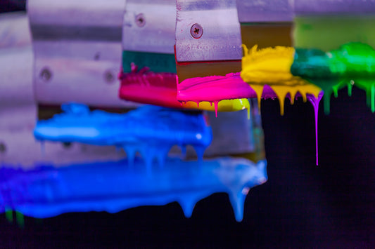Brightly coloured inks dripping from hanging squeegees used in screen printing